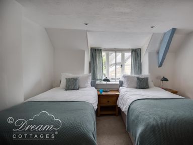 A bedroom with two single beds with green blankets and pillows a window with green curtains and wooden bedside tables with lamps at Lilac Cottage Burton Bradstock