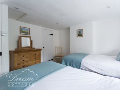A bedroom with two single beds a wooden dresser a chair and framed pictures at Lilac Cottage Burton Bradstock