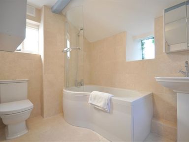 A bathroom with a toilet a bathtub with a glass shower screen and a sink at Lilac Cottage in Burton Bradstock