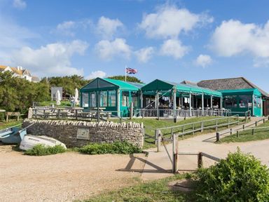 An outdoor seating area with green tent covers and boats near a stone wall at Lilac Cottage in Burton Bradstock