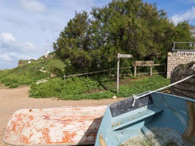 A small boat on a dirt path near a green hill and trees with wooden signs and a stone wall