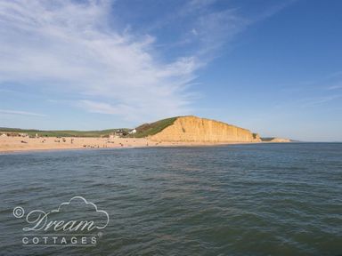 A beach with people near cliffs and water at Lilac Cottage in Burton Bradstock