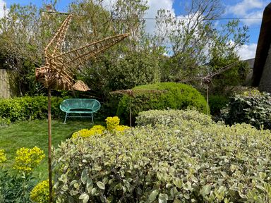 A garden with woven bird sculptures and a green chair at Lilac Cottage in Burton Bradstock