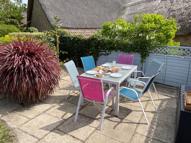 An outdoor patio with a glass table set with plates and food surrounded by colorful chairs at Lilac Cottage in Burton Bradstock