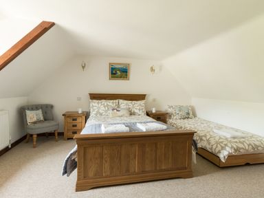 A bedroom with a double bed and a single bed with bedside tables and a gray chair at Little Forge in West Lulworth