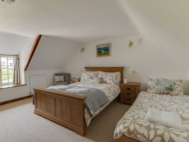 A bedroom with a double bed and a single bed with bedside tables and a chair at Little Forge in West Lulworth