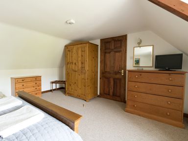A bedroom with wooden furniture including a wardrobe chest of drawers a bed a small bench and a television on a dresser at Little Forge in West Lulworth