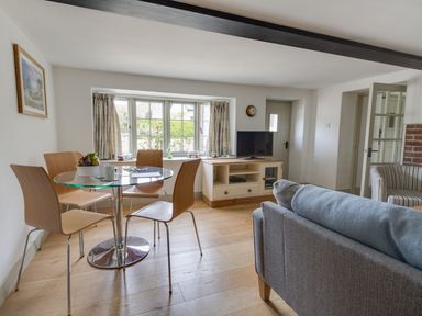 A living room with a glass dining table and wooden chairs a television on a wooden cabinet and a sofa at Little Forge in West Lulworth