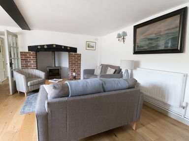 A living room with a gray sofa two armchairs a wooden floor a brick fireplace and a painting of a ship at Little Forge in West Lulworth