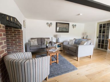 A living room with two grey sofas a striped armchair wooden coffee table and a brick fireplace at Little Forge in West Lulworth