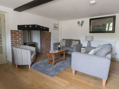 A living room with grey sofas a striped armchair a wooden coffee table a brick fireplace and a framed picture at Little Forge in West Lulworth
