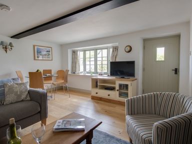 A living room with a sofa striped armchair glass dining table and television at Little Forge in West Lulworth