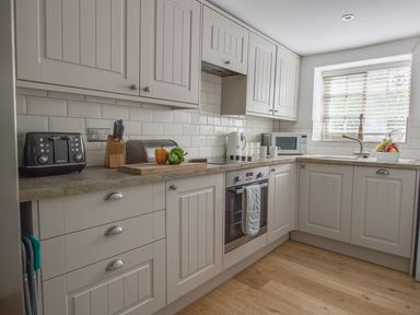 A kitchen with white cabinets countertop appliances and a window with blinds at Little Forge in West Lulworth