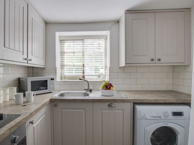 A kitchen with a sink under a window a microwave on the counter a washing machine and cabinets at Little Forge in West Lulworth