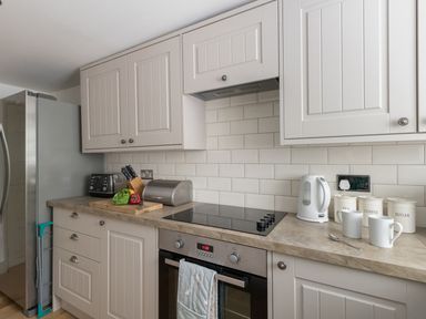 A kitchen countertop with a stove, oven, toaster, kettle, mugs, canisters labeled tea coffee sugar, cutting board with vegetables and knives at Little Forge in West Lulworth