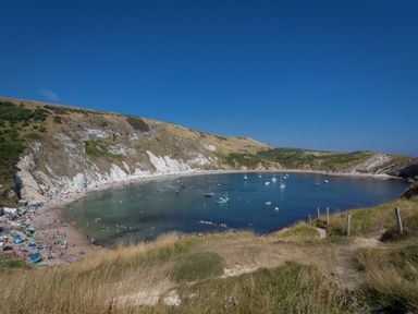 A coastal bay with boats anchored in the water and people on a beach at Little Forge in West Lulworth