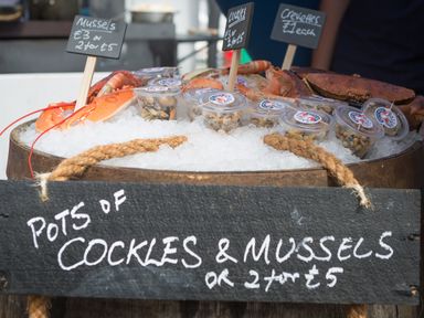 A display of seafood including pots of cockles and mussels on ice with price signs at Little Forge in West Lulworth