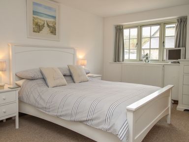 A bedroom with a white bed frame striped bedding two bedside tables lamps window with curtains and a chest of drawers at Little Forge West Lulworth