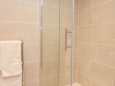 A shower area with glass door and a towel rack with white towels in a bathroom at Little Forge in West Lulworth