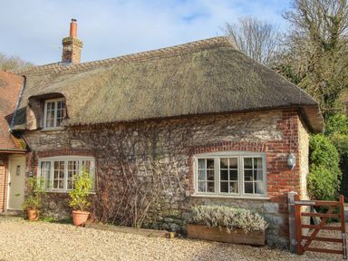 A stone cottage with a thatched roof and a wooden gate at Little Forge in West Lulworth