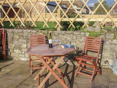 A patio area with a wooden table and chairs a bottle of wine two glasses and a book at Little Forge in West Lulworth