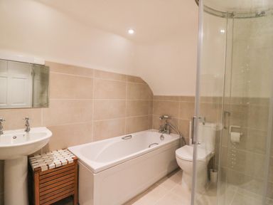 A bathroom with a pedestal sink wooden storage bench bathtub toilet and glass shower enclosure at Little Forge in West Lulworth