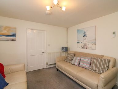 A sitting room with two beige sofas cushions paintings on walls a blue lamp radiator and a door at Lobster Cottage Brewers Quay Harbour