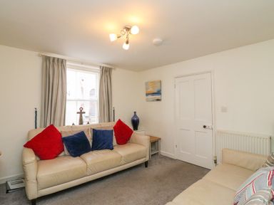 A living room with two beige sofas and colorful cushions at Lobster Cottage in Brewers Quay Harbour