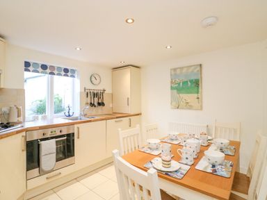 A kitchen with a wooden dining table set with bowls and mugs and cream cabinets at Lobster Cottage in Brewers Quay Harbour