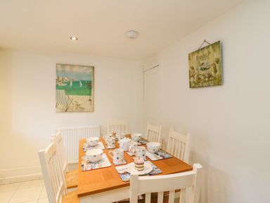 A dining room with a wooden table set with cups and bowls and white chairs at Lobster Cottage in Brewers Quay Harbour