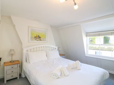 A bedroom with a white bed frame bedside tables with lamps rolled towels on the bed and a window at Lobster Cottage Brewers Quay Harbour