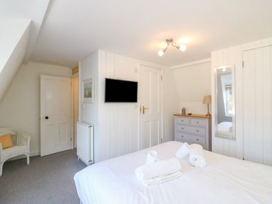 A bedroom with a bed and rolled towels a chest of drawers a chair and a wall-mounted TV at Lobster Cottage Brewers Quay Harbour