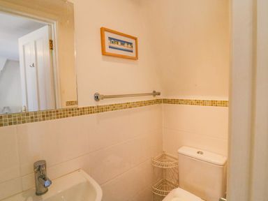 A small bathroom with a sink, toilet, mirror, towel rail, and a framed picture on the wall at Lobster Cottage Brewers Quay Harbour