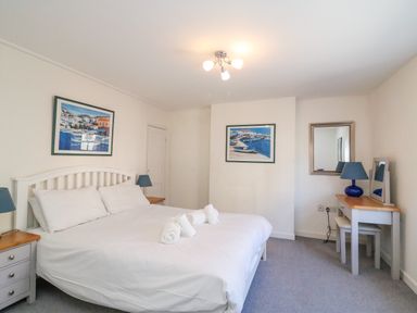 A bedroom with a double bed two bedside tables lamps a dressing table mirror and framed pictures on walls at Lobster Cottage in Brewers Quay Harbour