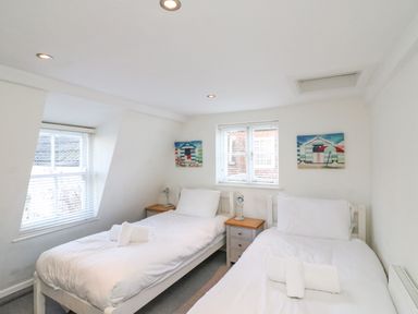 A bedroom with two single beds bedside tables and lamps under windows at Lobster Cottage in Brewers Quay Harbour