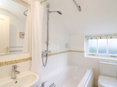 A bathroom with a bathtub shower combination a white sink and a toilet with a window above at Lobster Cottage in Brewers Quay Harbour