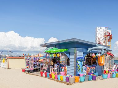 A beach shop selling inflatables toys buckets and flip flops with a playground in the background at Lobster Cottage in Brewers Quay Harbour