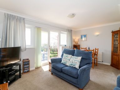 A living room with a blue sofa a dining table wooden cabinet and a television near glass doors at Lookout in Cove Castle