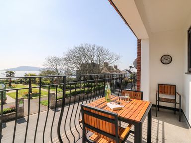A balcony with a wooden table and chairs overlooking a garden and street with a view of the sea at Lookout in Cove Castle