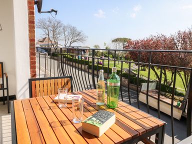 An outdoor balcony with a wooden table chairs a book two glasses a bottle of tonic water and a green bottle at Lookout in Cove Castle