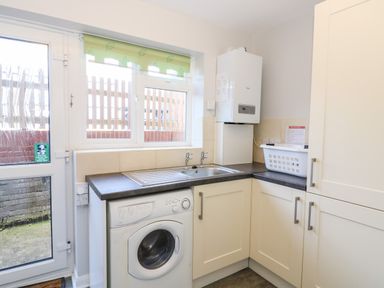 A laundry room with a washing machine sink countertop cabinets and a window at Lookout in Cove Castle