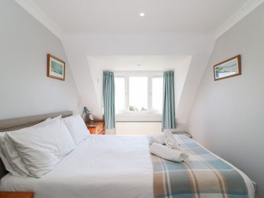 A bedroom with a bed with white linens and a plaid blanket beside a window with blue curtains at Lookout in Cove Castle