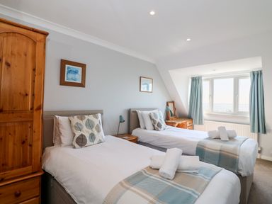 A bedroom with two single beds wooden wardrobe nightstand and window with curtains at Lookout in Cove Castle