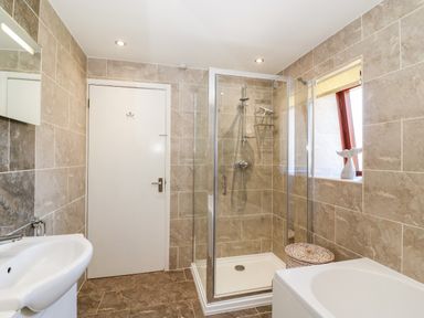 A bathroom with a shower enclosure a sink a bathtub and a wicker laundry basket at Lookout in Cove Castle