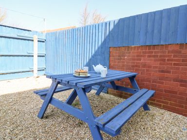 An outdoor area with a blue wooden picnic table set with a teapot, cups, and muffins surrounded by a blue wooden fence and a red brick wall at Lookout in Cove Castle