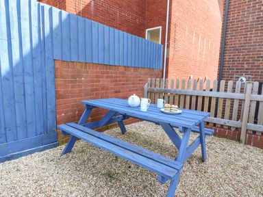 A blue picnic table with tea set and cupcakes on gravel next to a red brick wall and blue wooden fence at Lookout in Cove Castle