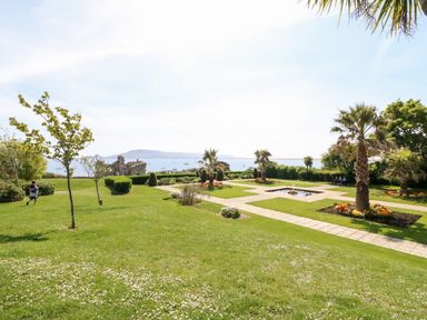 A garden with pathways, palm trees, flower beds and a view of the sea with boats at Cove Castle