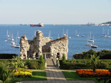 A garden with flowers and a pathway leading to castle ruins by the sea with boats and ships in the water at Lookout in Cove Castle