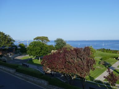 A coastal park with trees benches and a paved pathway overlooking the sea with boats at Cove Castle
