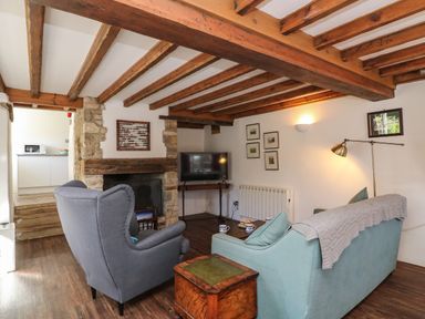A living room with wooden beams a fireplace a blue sofa and a grey armchair at Lychgate Cottage in Osmington
